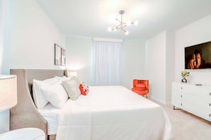 A modern hotel room with a large bed, a desk, a chair, and a ceiling light fixture. - 7BR Windsor Cay Home w/ Pool & Game Room (Clermont)