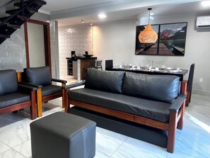 Un salon moderne comprenant un canapé, des fauteuils, une table basse et un coin repas avec une table dressée pour quatre personnes.