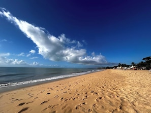 Une plage où l’on voit des empreintes de pas menant à l’eau, un ciel dégagé et une côte lointaine parsemée de constructions.