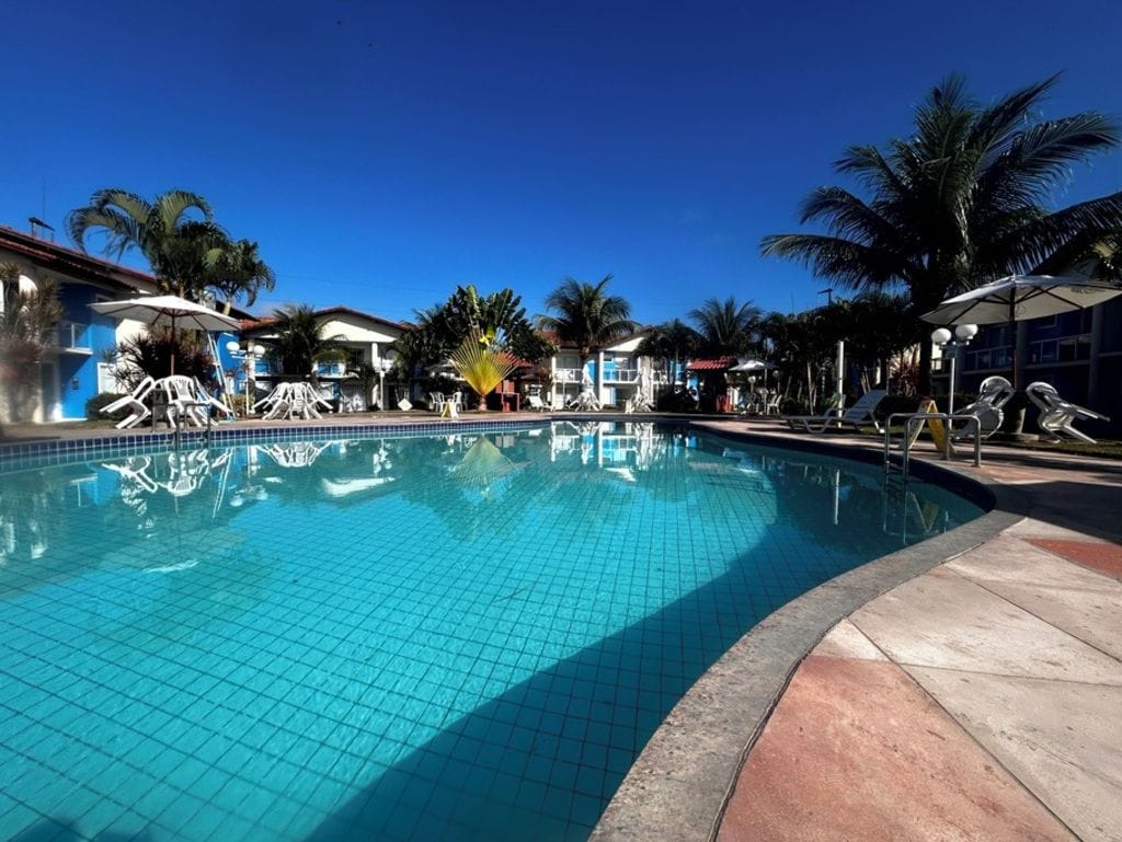 A swimming pool with tiled edges, surrounded by palm trees and buildings.