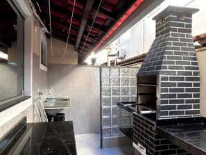 A kitchen with a brick oven, a sink, and a window. - Cj17MSII-3D Porto Seguro Piscina/Sauna/ArConforto (Porto Seguro)