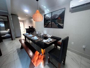 Un coin repas avec une table noire dressée pour quatre personnes, un banc et une suspension.