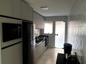 Une cuisine avec un réfrigérateur, une cuisinière et un évier noirs. Il y a une fenêtre donnant sur l’extérieur.