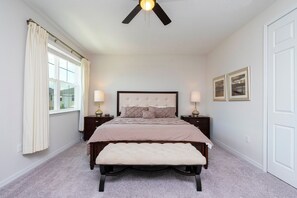 A bedroom with a bed, bedside tables, a bench, a ceiling fan, and a window with curtains. - Modern 7BR Villa Pool + Resort Amenities (Kissimmee)