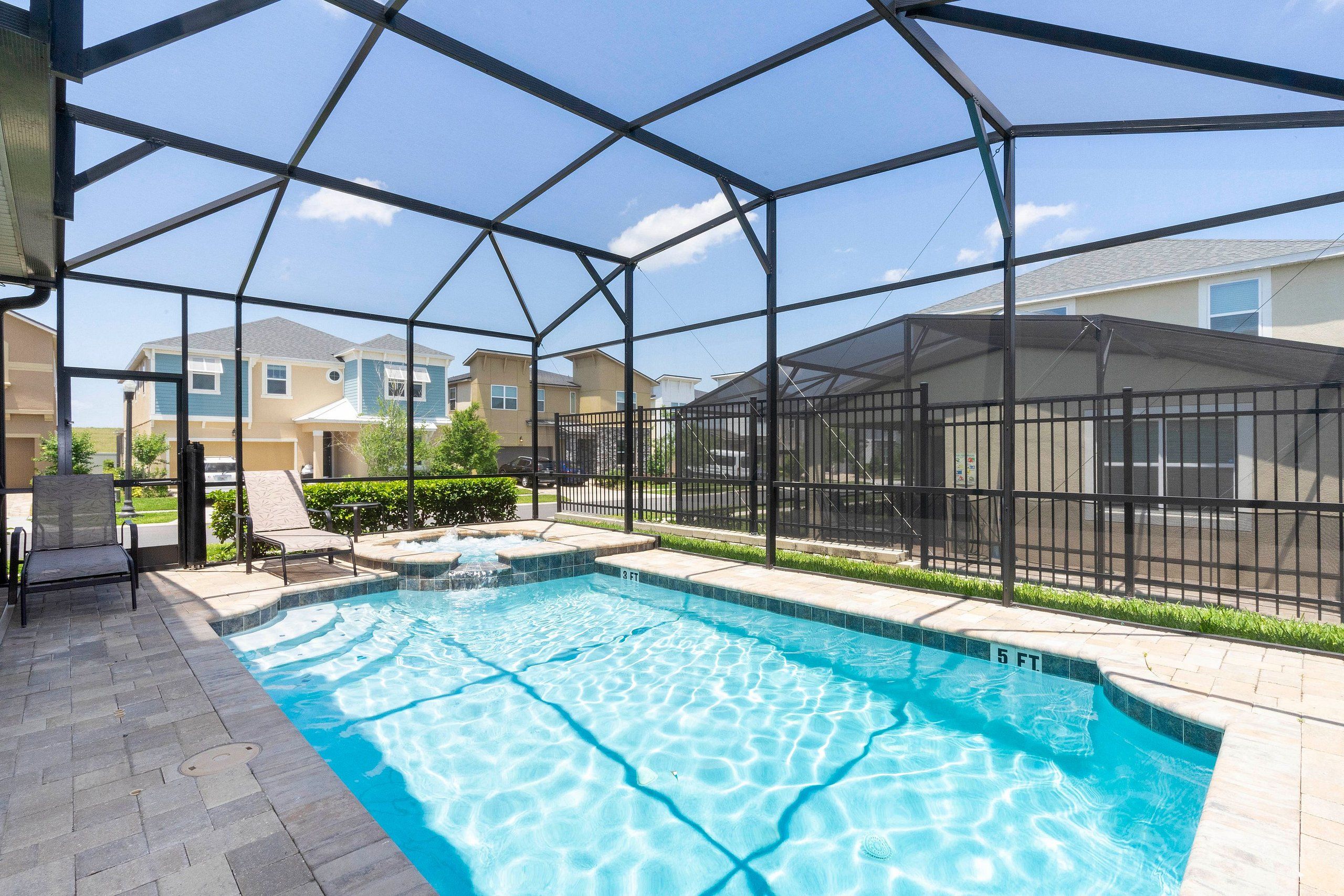 A swimming pool with a 5 ft depth, surrounded by a covered area with chairs and a small waterfall feature.