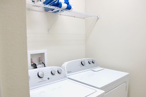 A laundry room with two white Whirlpool washers and dryers, a metal shelf above the dryers, and a small white cabinet with bottles. - 8br/6ba Luxury Villa, Private Pool, Disney (Kissimmee)