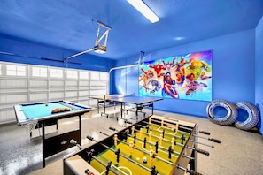 Ein Spielzimmer mit Billardtisch, Kicker und einer großen Wandmalerei von Superhelden.