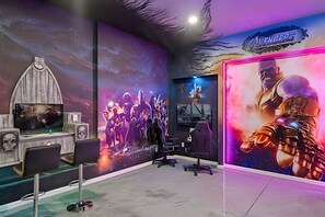 Ein Spielzimmer mit großem Bildschirm, Gaming-Stühlen und einer Wandmalerei, die einen Charakter aus einer bekannten Filmreihe zeigt.