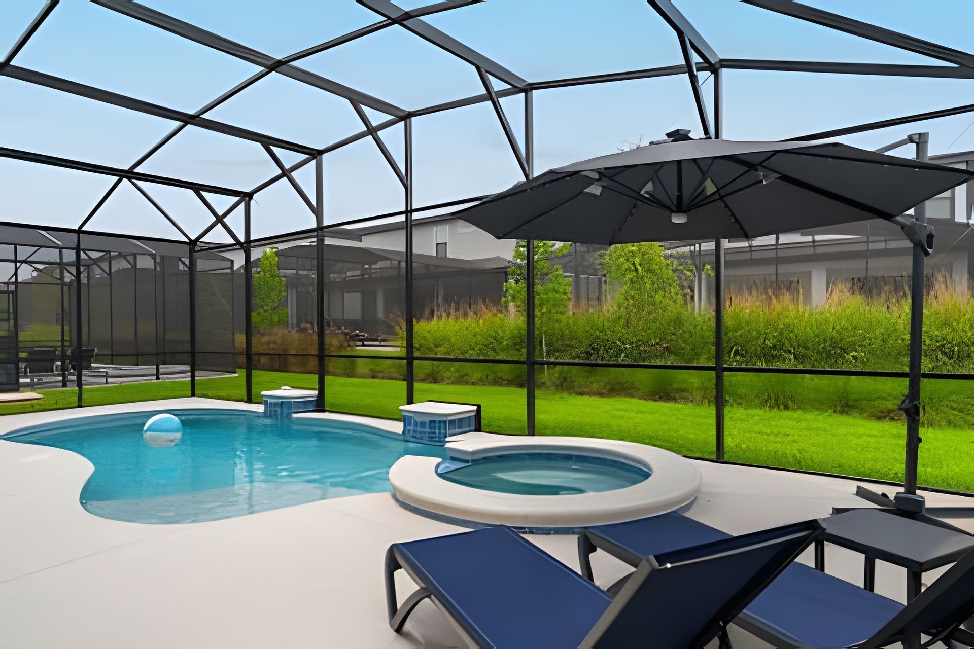 An indoor swimming pool with a glass enclosure, lounge chairs, and a hot tub.