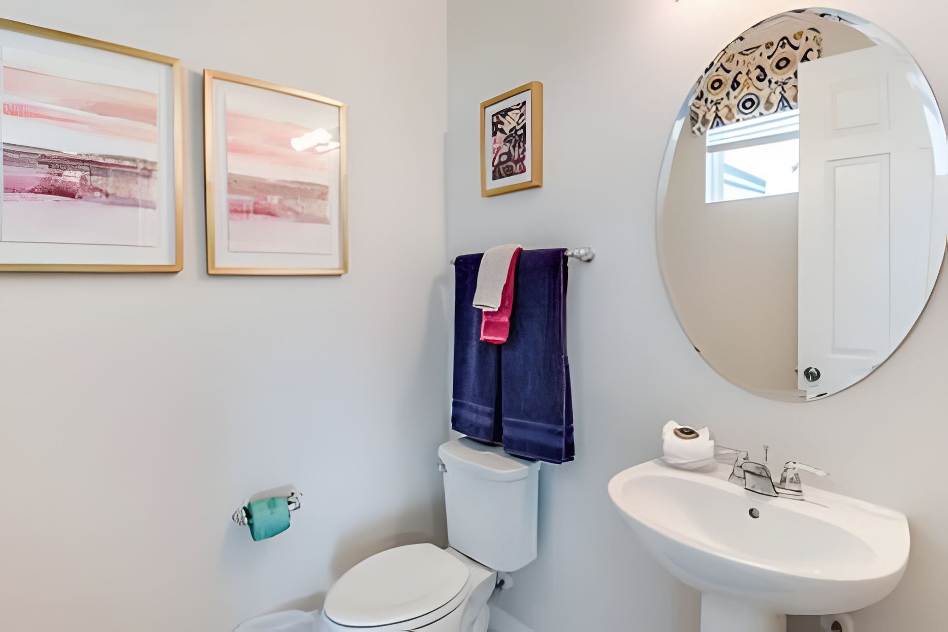 A bathroom with a toilet, sink, and two framed pictures on the wall.
