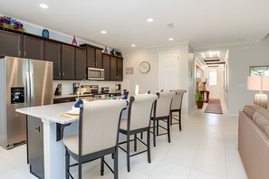 A modern kitchen with dark cabinets, a stainless steel refrigerator, a microwave, and a dining area with a white table and four chairs. - Disney 6BR Villa w/ Pool & Themed Rooms (Kissimmee)