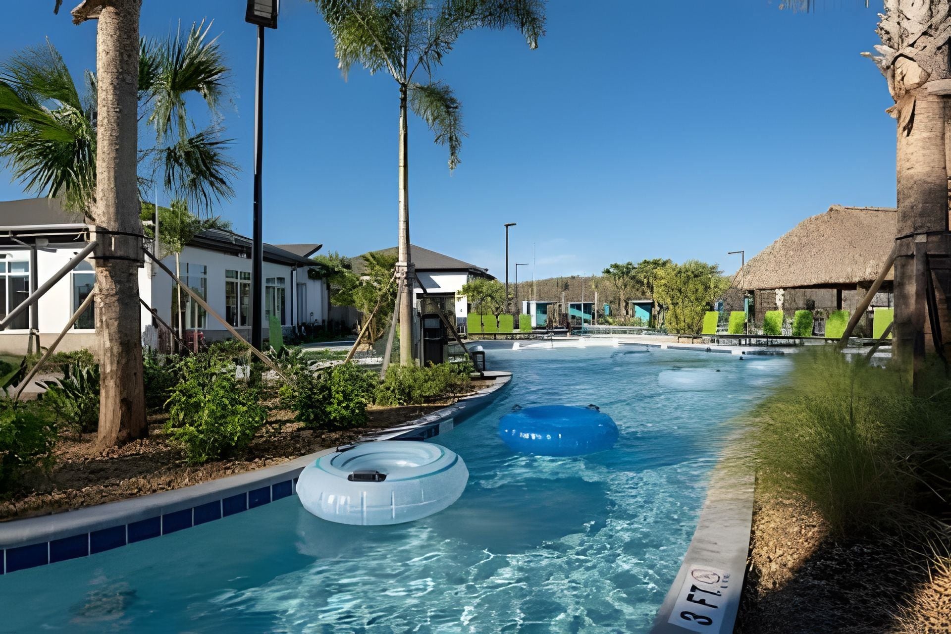 A swimming pool with inflatable rings, surrounded by palm trees and buildings.