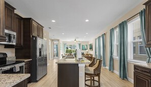 A modern kitchen with dark wood cabinets, stainless steel appliances, and a central island with bar stools. - Luxury 8BR Villa w/ Pool, Game & Theater Room (Kissimmee)