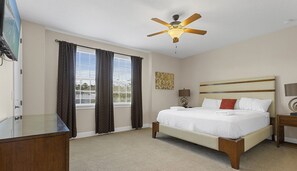 A hotel room with a bed, a ceiling fan, a window with curtains, a wall-mounted lamp, and a painting. - Luxury 8BR Villa w/ Pool, Game & Theater Room (Kissimmee)