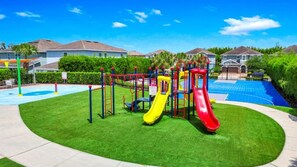 A playground with slides and climbing structures, surrounded by well-maintained grass and a pool. - Luxury 8BR Villa w/ Pool, Game & Theater Room (Kissimmee)