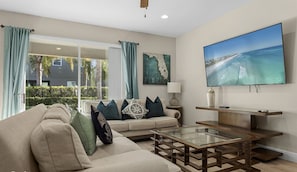 A living room with a sofa, coffee table, and a flat-screen TV mounted on the wall. - Luxury 8BR Villa w/ Pool, Game & Theater Room (Kissimmee)