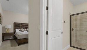 Une chambre à coucher comprenant un lit, une table de chevet, une lampe et une porte donnant accès à une salle de bain.