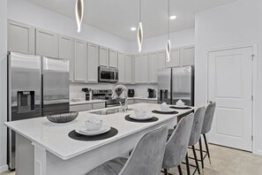 Una cocina moderna con armarios blancos, electrodomésticos de acero inoxidable, una isla central con asientos e iluminación colgante.