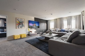 A modern living room with a large flat-screen TV, a sofa set, a coffee table, and a painting on the wall. - Storey Lake 7BR Villa w/ Pool, Spa & Game Room (Kissimmee)