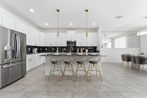 A modern kitchen with white cabinets, stainless steel appliances, and a central island with bar stools. - 6BR / 5BA Villa w/ Pool & Spa Storey Lake (Kissimmee)