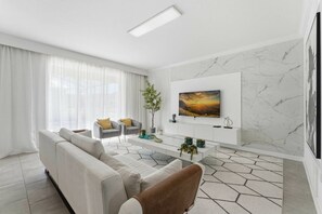 A modern living room with a sofa, armchairs, a coffee table, and a TV mounted on the wall. - 6BR / 5BA Villa w/ Pool & Spa Storey Lake (Kissimmee)