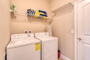 A laundry area with two washing machines, a drying rack, and folded towels on a shelf. - 6BR Solterra Home w/ Pool + Resort Access (Davenport)