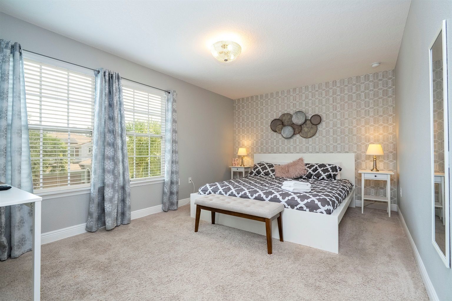 A bedroom with a large bed, bedside tables with lamps, a bench, and a wall with a geometric pattern.