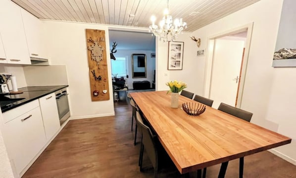 A modern kitchen with white cabinets, a wooden dining table, and a chandelier. - BREITHORN – SPACIOUS 3-BEDROOM APARTMENT IN CENTRAL ZERMATT (Zermatt)