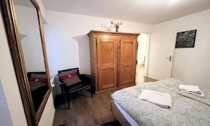 A bedroom with a bed, a wooden wardrobe, a chair, and a mirror. - BREITHORN – SPACIOUS 3-BEDROOM APARTMENT IN CENTRAL ZERMATT (Zermatt)