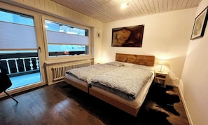 A bedroom with a bed, a window, a radiator, a nightstand, and a painting on the wall. - BREITHORN – SPACIOUS 3-BEDROOM APARTMENT IN CENTRAL ZERMATT (Zermatt)