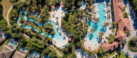 An aerial view of a resort with multiple swimming pools, palm trees, and a tennis court.