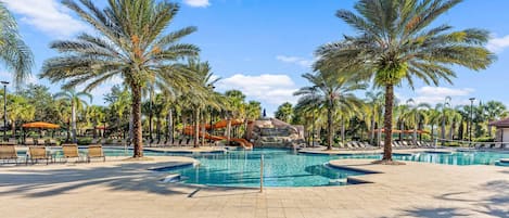 A pool area with multiple swimming pools, lounge chairs, palm trees, and a rock formation in the background.