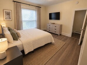 A bedroom with a bed, bedside table, lamp, dresser, television, and a door. - 35 Fairview - Recent reno, 1st floor apt, near ASV (Oneonta)