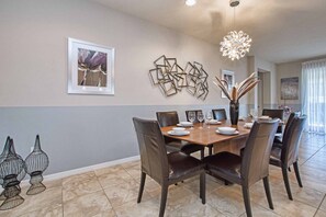 A dining area with a wooden table, six chairs, and a chandelier. - 8BR Home for 18 w/ Private Pool Windsor (Kissimmee)