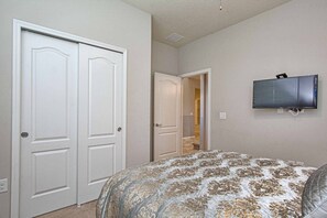 A bedroom with a bed, a television mounted on the wall, and two closed doors. - 8BR Home for 18 w/ Private Pool Windsor (Kissimmee)