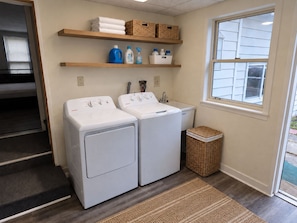 A laundry room with two front-loading washing machines, a sink, and shelves above holding towels and laundry supplies. - Recent renovation, 2nd floor apt, near ASV (Oneonta)