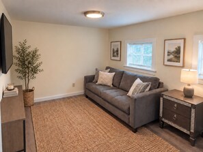 A living room with a sofa, a side table with a lamp, a wall-mounted TV, and framed pictures on the wall. - Recent renovation, 2nd floor apt, near ASV (Oneonta)