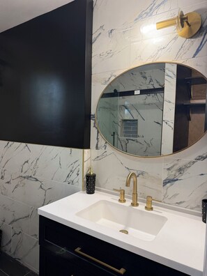 A bathroom with a white sink, gold faucets, a black cabinet, and a marble backsplash. - 2 Bdrm, Total renovation, overlooking Canadarago (Richfield Springs)