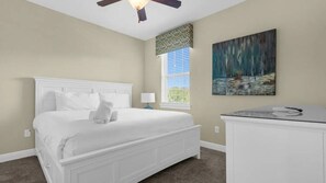 A bedroom with a white bed, a nightstand, a ceiling fan, a window with blinds, and a painting on the wall. - 7BR Themed Villa w/ Pool 6mi Disney (Kissimmee)