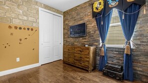 A room with a brick wall, a wooden dresser, a white door, and a window with blue curtains. - 7BR Themed Villa w/ Pool 6mi Disney (Kissimmee)