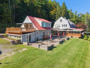 A two-story building with a red roof, a balcony, and a covered patio area with outdoor seating. - Hatch's Entire Flock  - 5 unit compound (Cooperstown)
