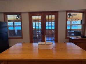A room with a wooden table, a white container, and a view of a wooden deck and outdoor seating through a glass door. - Hatch's Entire Flock  - 5 unit compound (Cooperstown)
