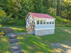 A small wooden cabin with a red roof, a porch, and a staircase leading up to the entrance. - Hatch's Coop - Awesome lake views, great studio cottage (Cooperstown)