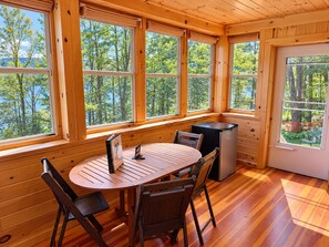A wooden cabin with a dining table and chairs, large windows, and a refrigerator. - Hatch's Coop - Awesome lake views, great studio cottage (Cooperstown)
