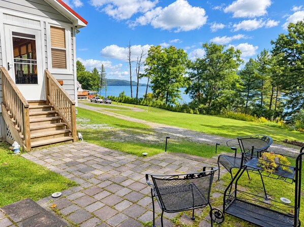 A house with a wooden staircase leading to a deck, a patio with a table and chairs, and a view of a lake. - Hatch's Coop - Awesome lake views, great studio cottage (Cooperstown)