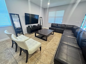 A modern living room with a sectional sofa, a coffee table, a TV, and a seating area with a chair. - 9BR Retreat for 20 w/ Game Room Champions Gate (Davenport)