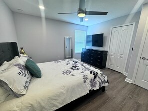 A bedroom with a bed, a ceiling fan, a dresser, a TV, and a door. - 9BR Retreat for 20 w/ Game Room Champions Gate (Davenport)