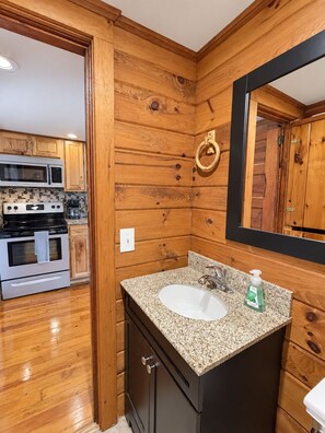 A wooden interior with a kitchen area featuring a stove, microwave, and cabinets. - Hatch's Roost -  Classic Otsego Camp, shared waterfront (Cooperstown)