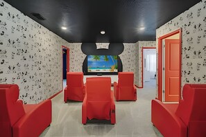 A room with a large flat-screen TV on the wall, red seating, and a Mickey Mouse-shaped ceiling light fixture. - Luxury 10br Resort Home w/ Pool & Movie Theater (Clermont)