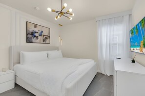 A modern bedroom with a large bed, a bedside table, a desk, and a painting on the wall. - Luxury 10br Resort Home w/ Pool & Movie Theater (Clermont)